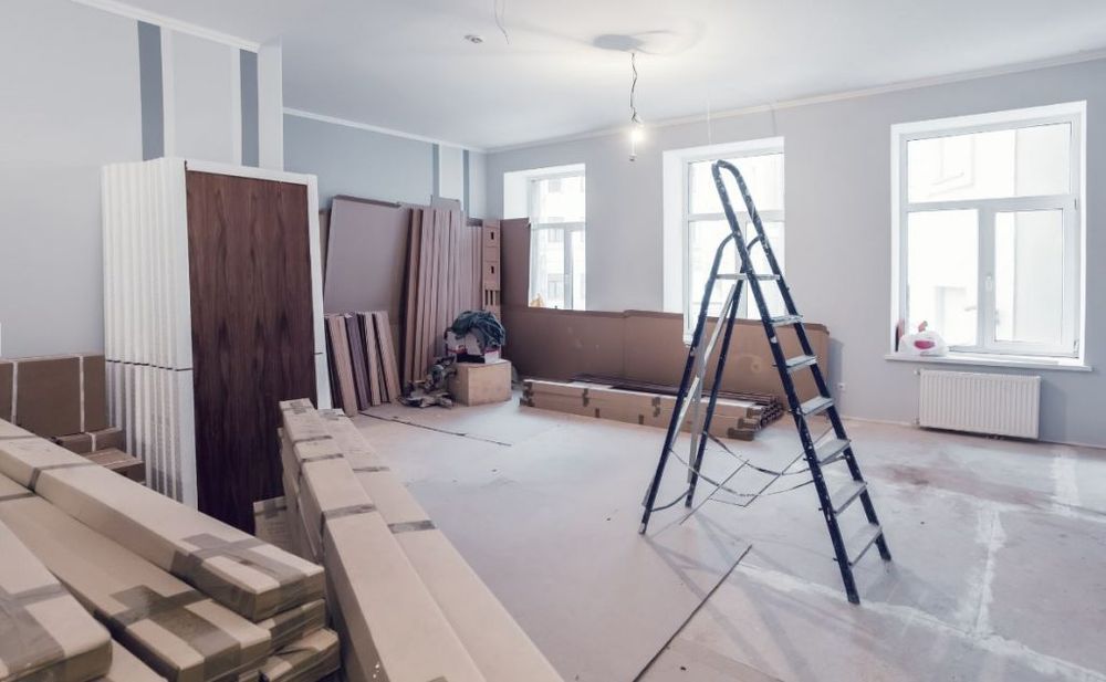 An interior room under renovation with stacked boxes, wood panels, and a stepladder