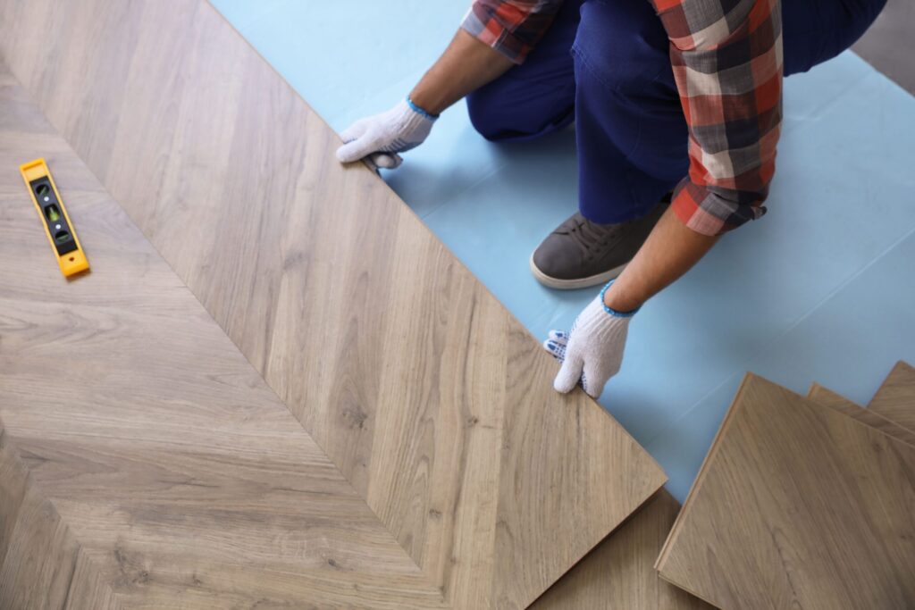 Worker installing wood-look laminate flooring planks in a herringbone pattern