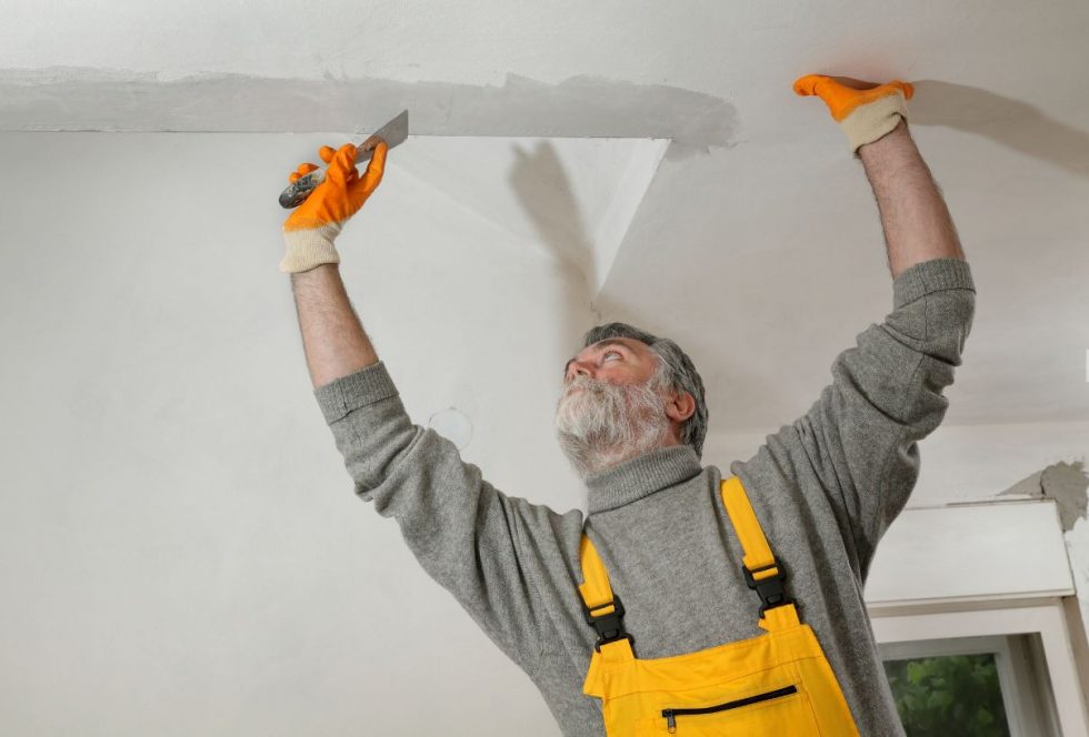 Technician sanding a finished drywall surface smooth before priming