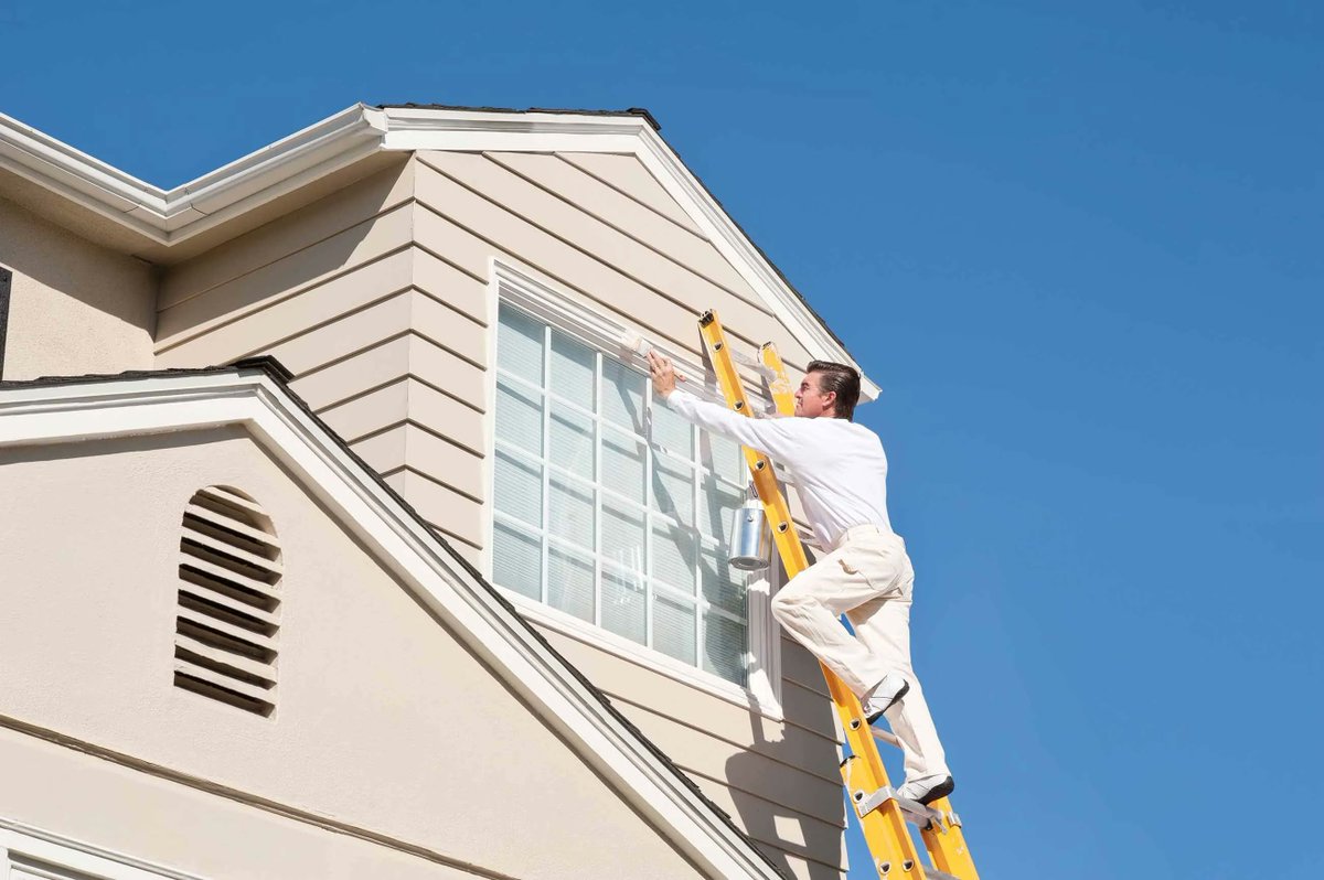 Painter working from a ladder on the upper siding and trim of a two-storey house
