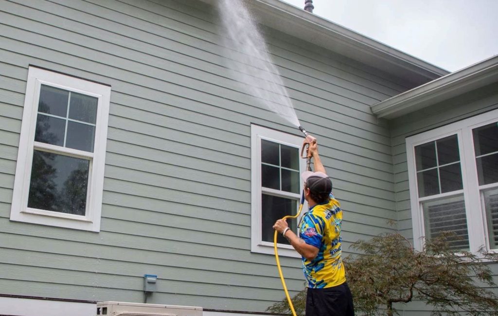 Technician soft washing the upper siding and trim of a residential property