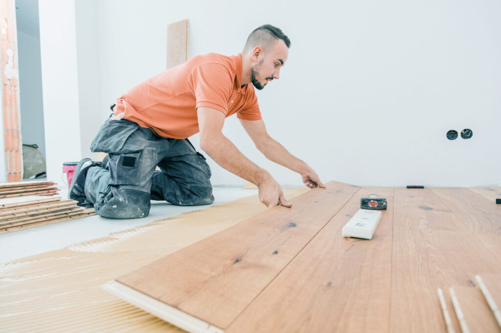 Flooring installer kneeling on the floor to lay wooden planks on adhesive