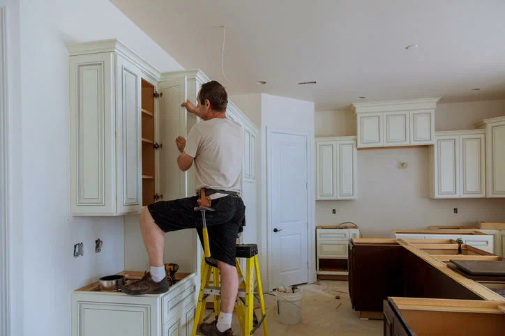 Carpenter on a ladder completing cabinetry and trim detail in a finished room
