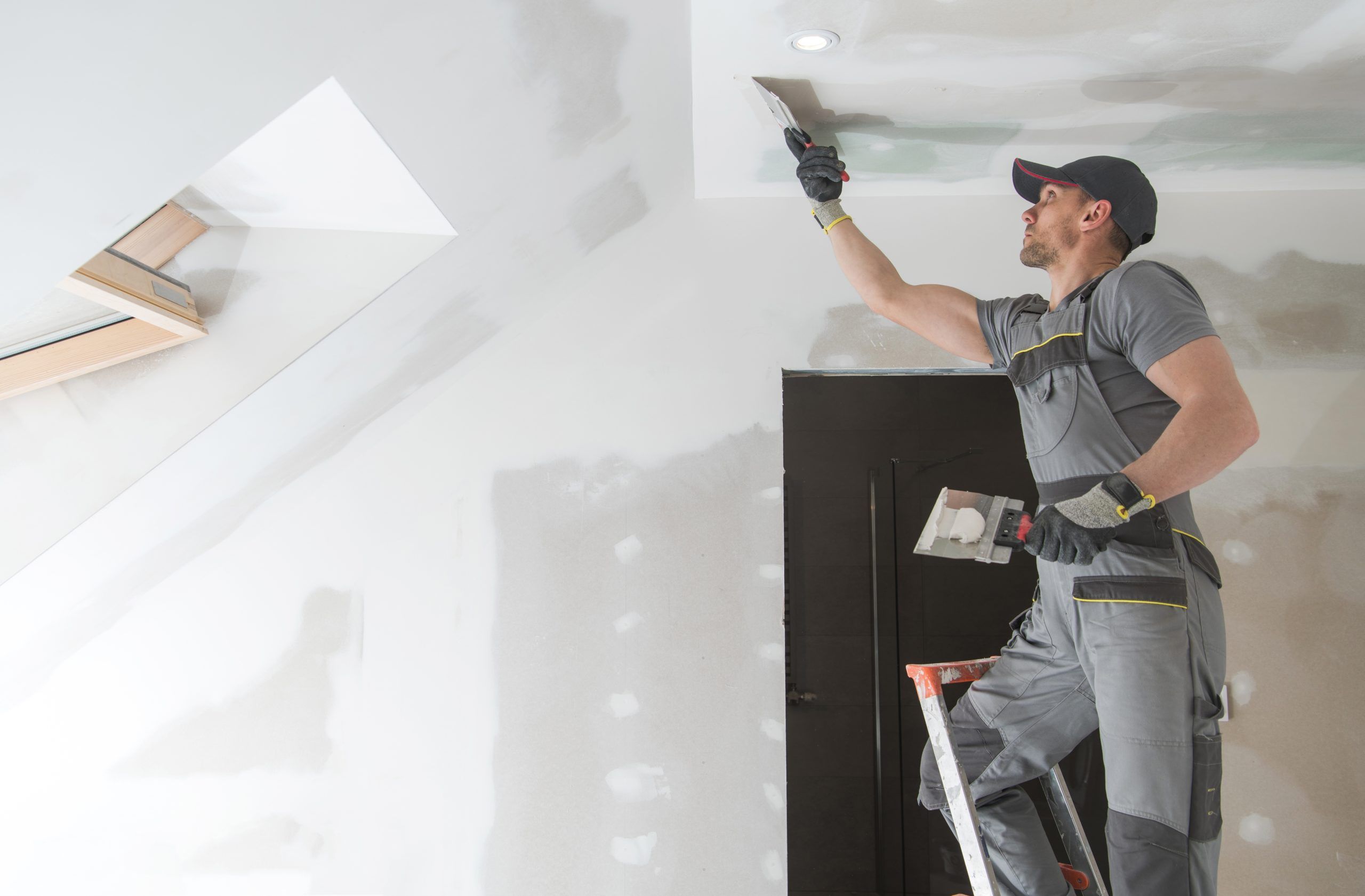 Drywall finisher taping and bedding a ceiling joint with a broad knife