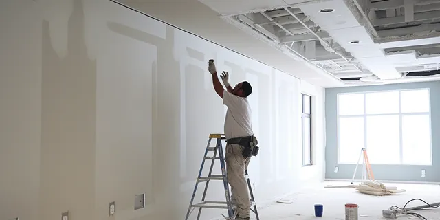 Prestige Home Experts crew member working on ceiling drywall from a ladder