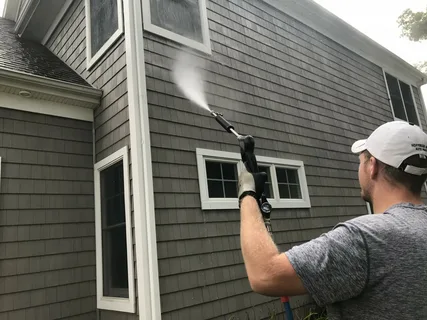 Prestige Home Experts operator rinsing exterior siding and window trim clean
