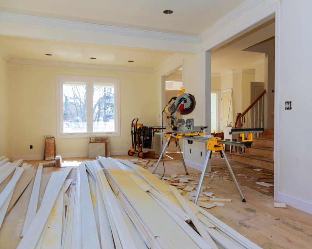 Miter saw setup and stacks of white trim boards inside a house under interior remodeling