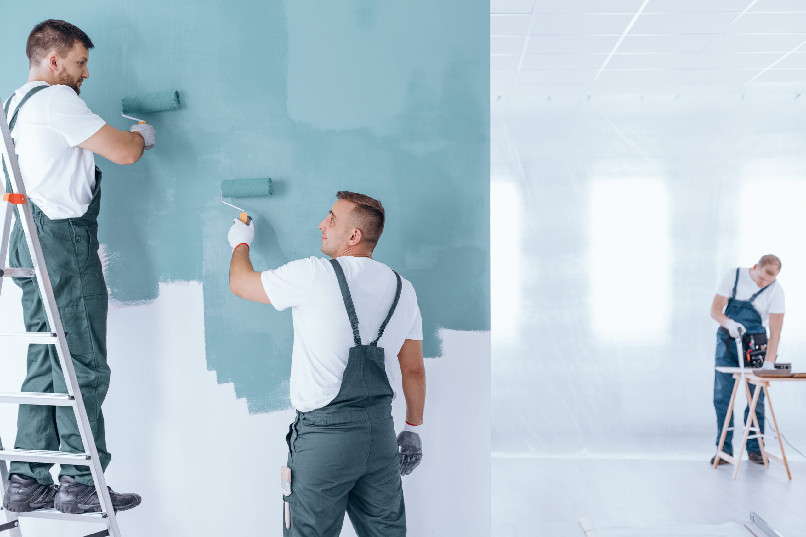 Painter applying a light blue finish coat to an interior wall in a prepared empty home