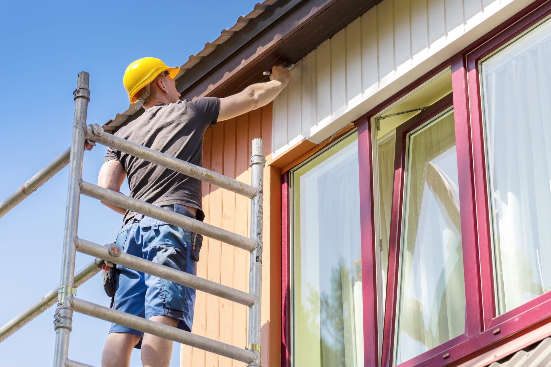 Crew member preparing and coating exterior siding from staging on a residential property